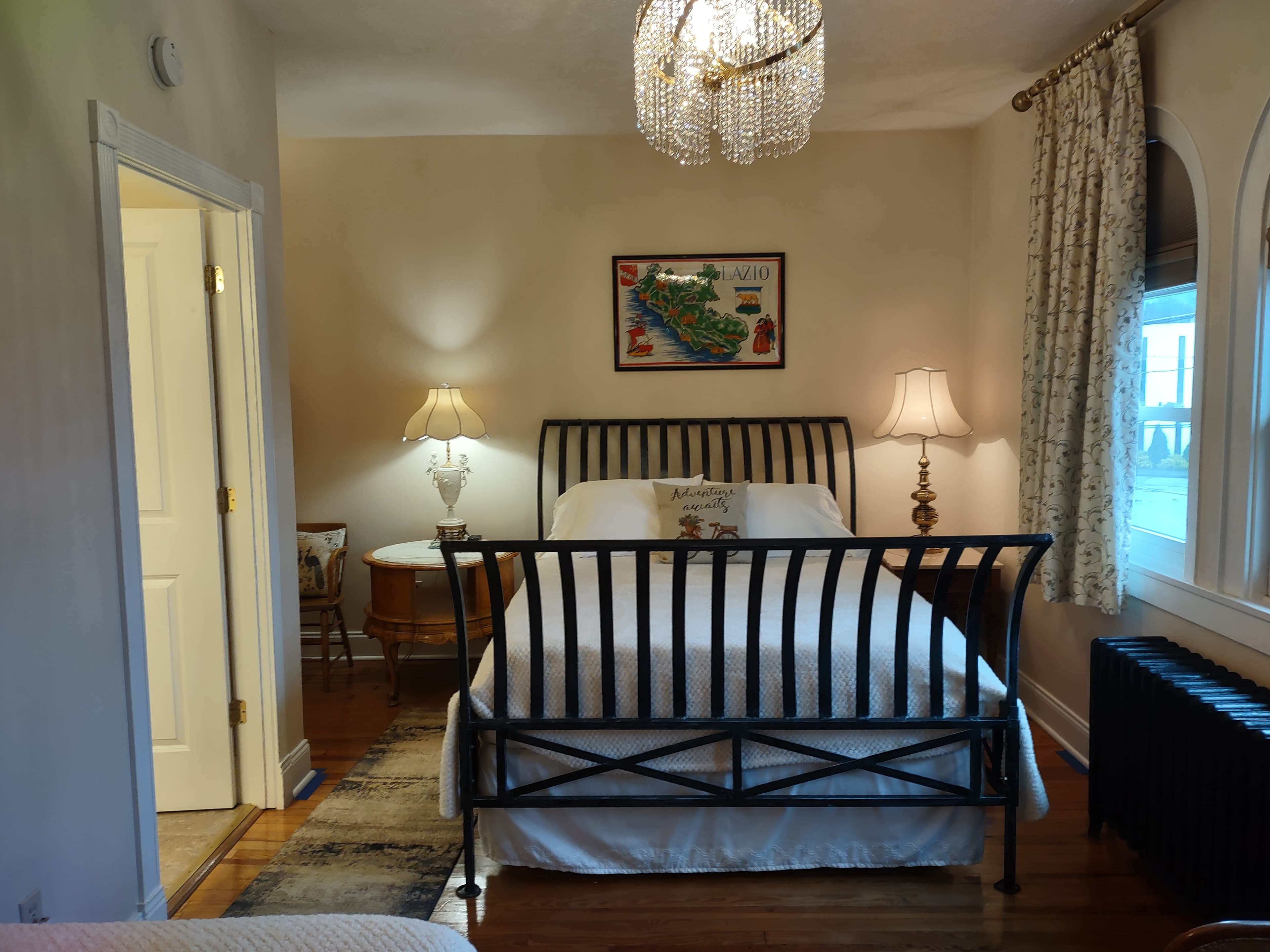 Night stands with lamps on both sides of iron sleigh queen bed, Tea Towel of Lazio Province framed above bed