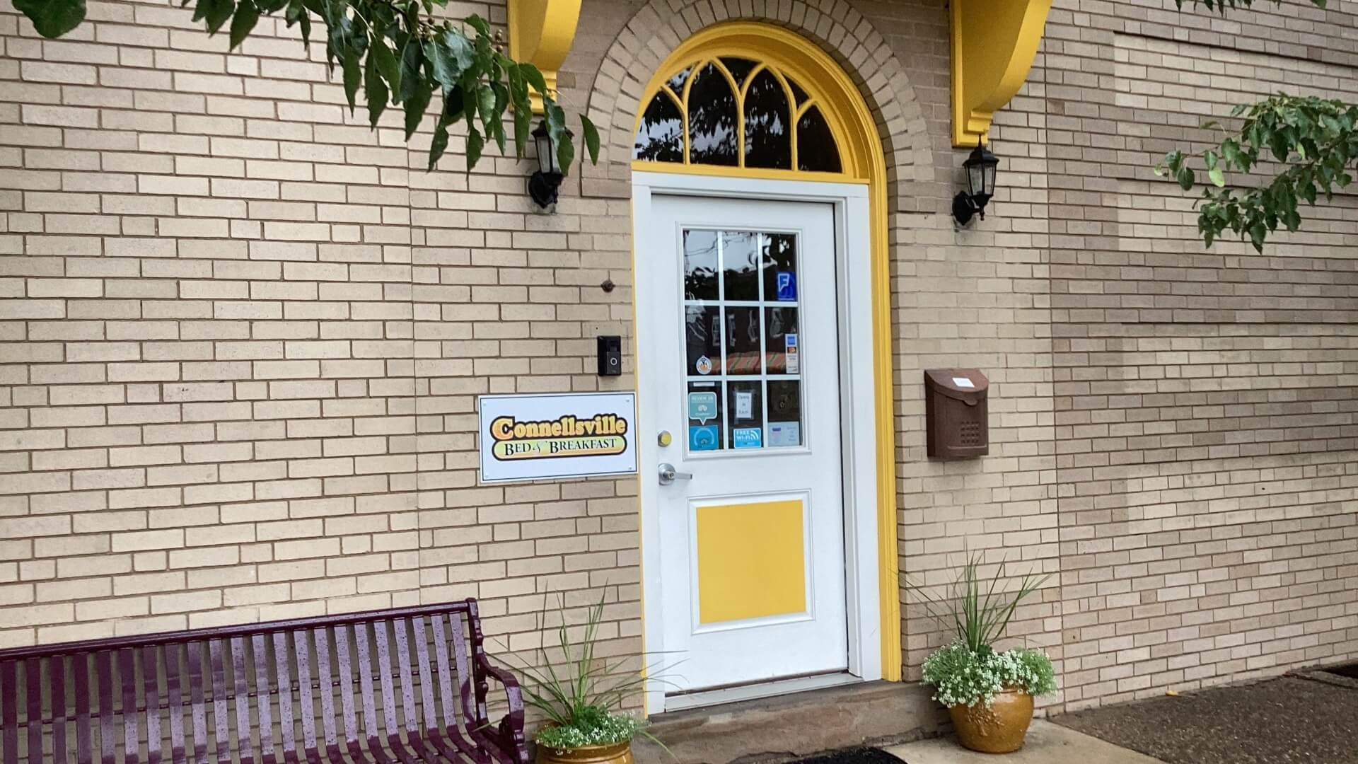 Front entrance of Conneautville with a white door, yellow accents, and a bench nearby.