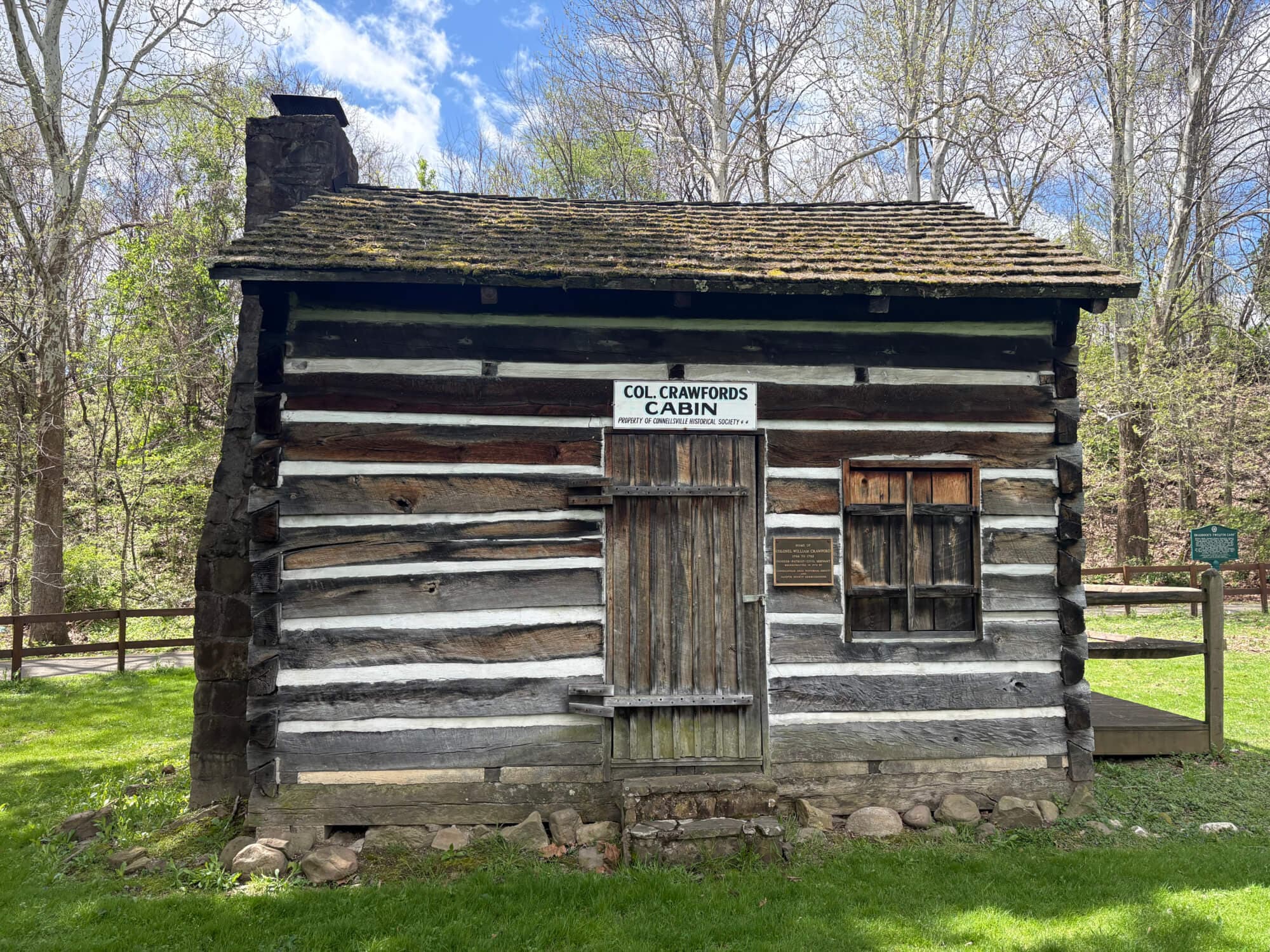 A historic log cabin labeled "Col Crawford's Cabin" surrounded by greenery and trees.