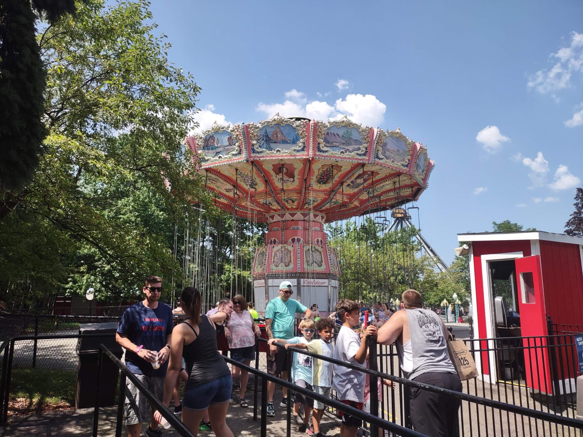 A colorful swing ride is seen in an amusement park with a line of people waiting in front.
