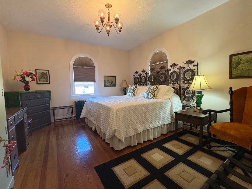 King bed with white quilted bedspread, headboard is arched metal frame with ivy vines, carpet with beige squares on black background