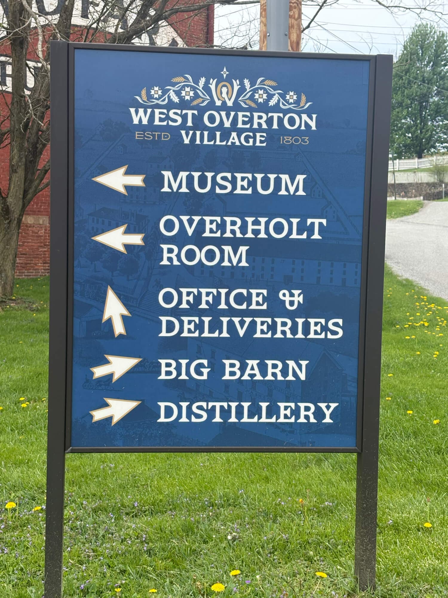 Signpost with directional arrows for the Museum, Overholt Room, Office & Deliveries, Big Barn, and Distillery in West Overton Village.