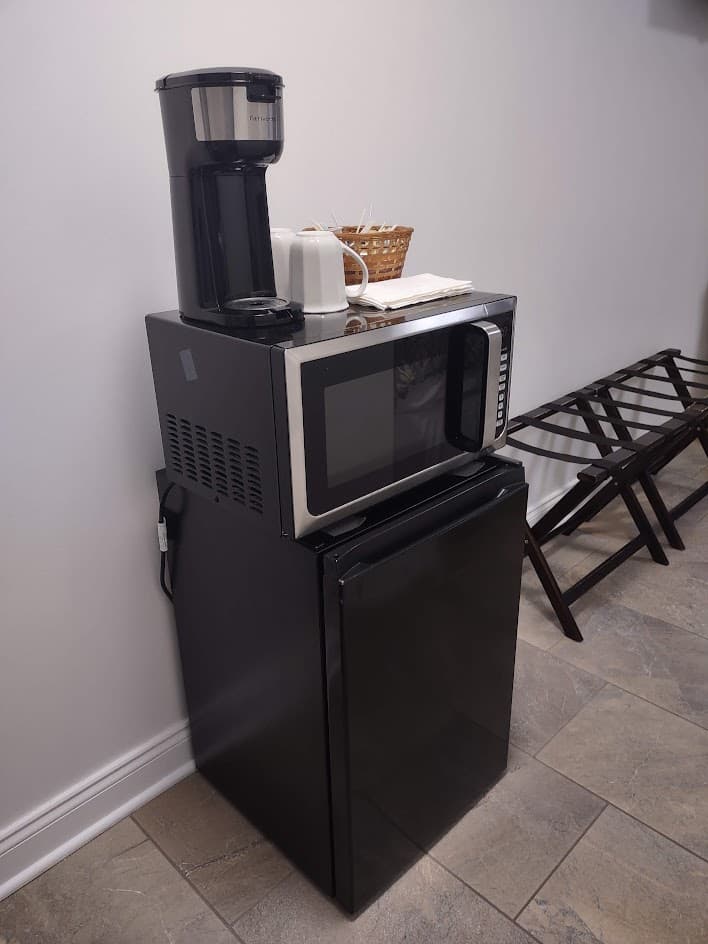 Coffee maker with cups and and basket of Keurig cups, assorted teas on top of black microwave and black mini-refrigerator