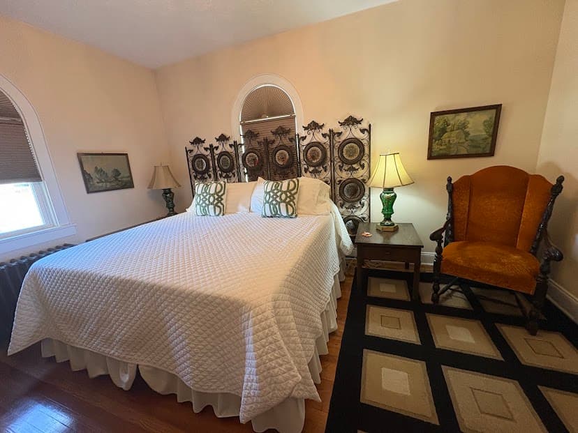King bed with arched headboard, antique chair and green lamp on both sides of bed