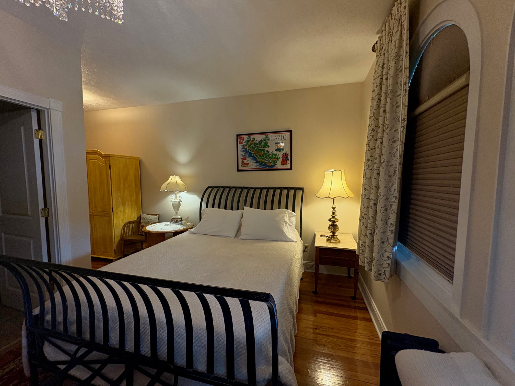 Night stands on both sides of sleigh iron Queen bed, wardrobe shown to the left of chair near night stand