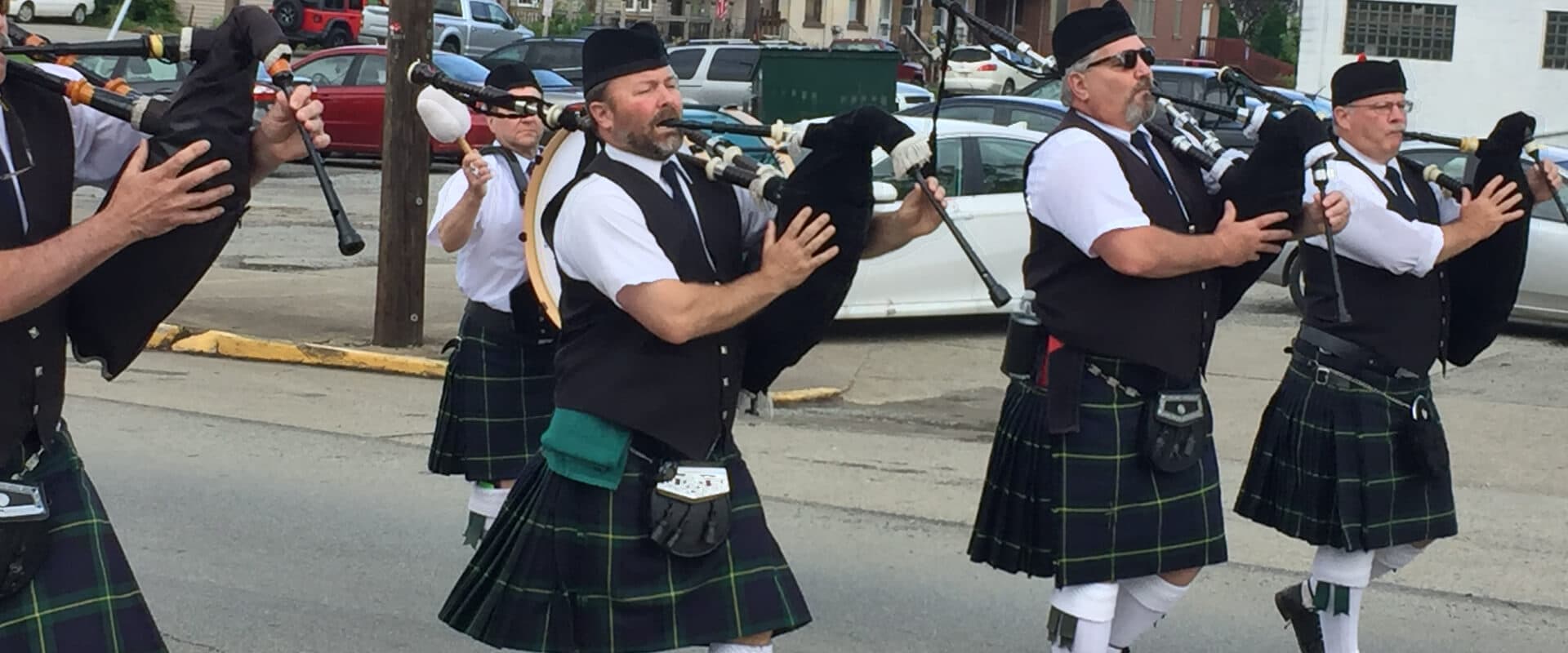 A group of men in kilts play bagpipes during a parade.