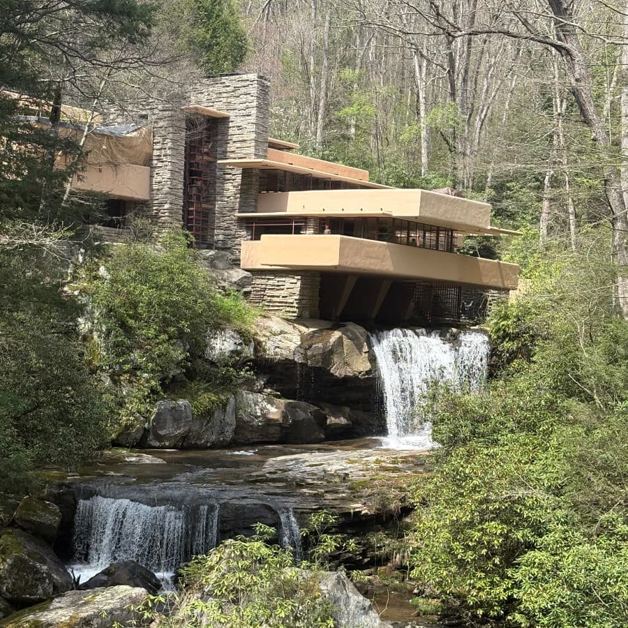 A modern house perched over a waterfall, surrounded by lush greenery.