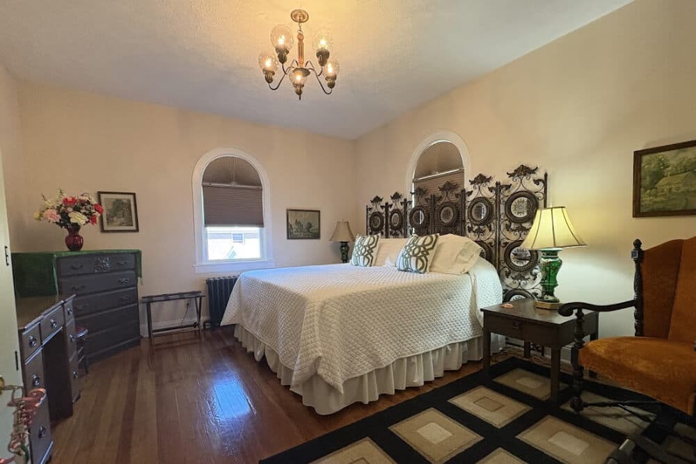 A cozy bedroom featuring two beds, decorative pillows, a chandelier, and vintage furniture.